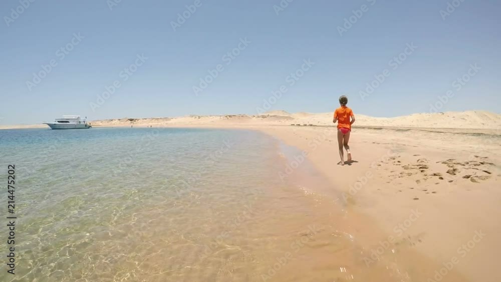 Little girl in swimwear running away on the sea beach in desert Little girl in swimwear running away on the sea beach in desert