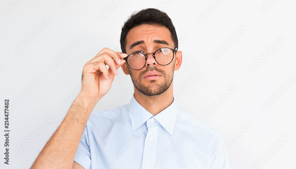 Closeup image of handsome bearded young male looking to the camera, touches rim of round spectacles, wears blue shirt, stands against studio background. People, business, health, emotions concept Closeup image of handsome bearded young male looking to the camera, touches rim of round spectacles, wears blue shirt, stands against studio background. People, business, health, emotions concept
