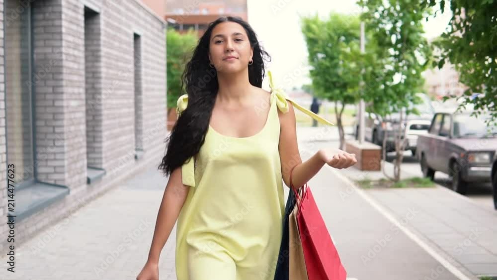 A beautiful young girl in a yellow dress is walking down the street after shopping having a good mood. slow motion. HD