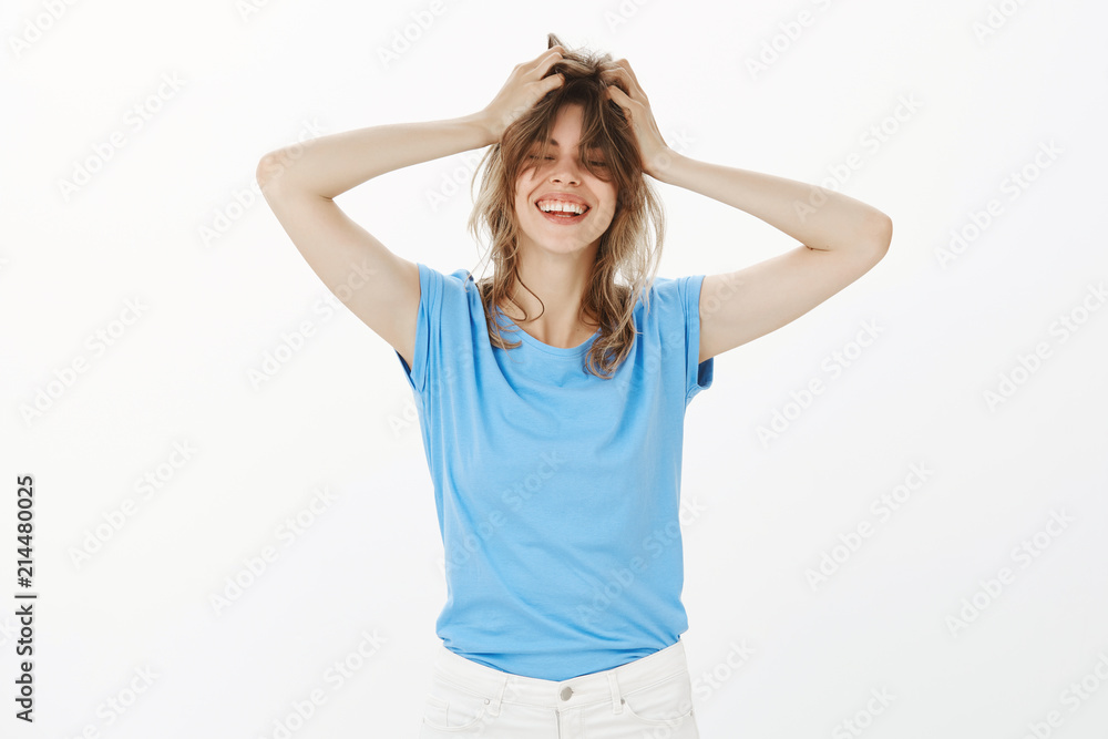Joyful bright european female in casual outfit, touching head and making hair messy, closing eyes and smiling broadly, feeling carefree and relaxed, enjoying bight sunny day on weekend