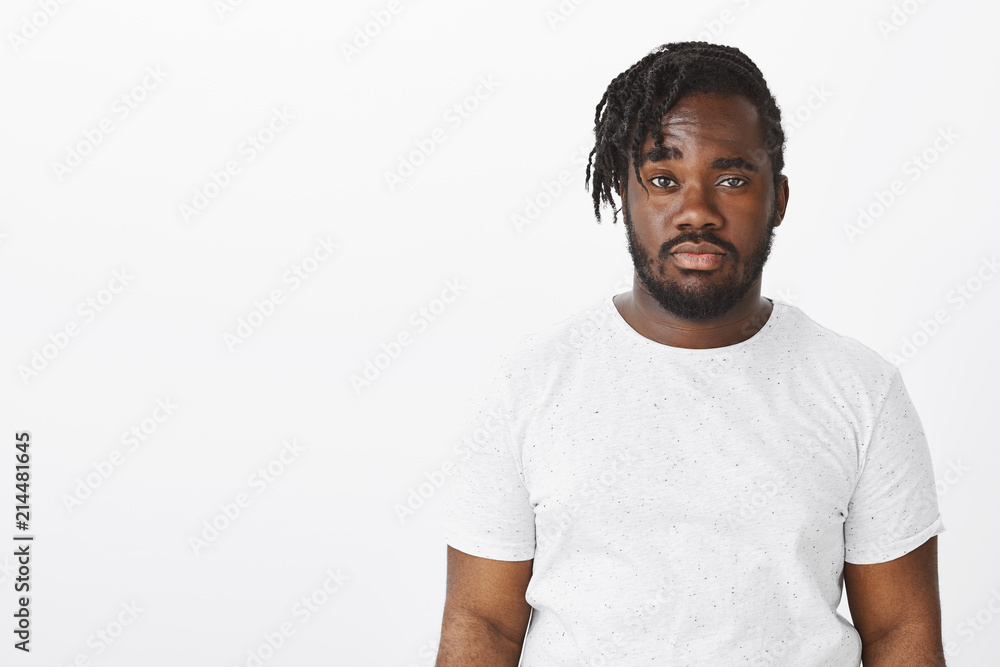 Waist-up shot of doubtful unimpressed dark-skinned man with stylish haircut, raising one eyebrown with doubt and staring seriously at camera, being careless and indifferent over white background Waist-up shot of doubtful unimpressed dark-skinned man with stylish haircut, raising one eyebrown with doubt and staring seriously at camera, being careless and indifferent over white background