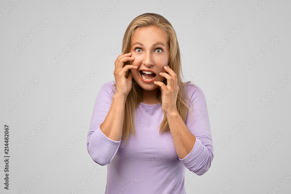 Woman with nervous expressions face, keeps hands near mouth and stare with big eyes against white background. Studio shot of frightened young woman, people and fear concept Woman with nervous expressions face, keeps hands near mouth and stare with big eyes against white background. Studio shot of frightened young woman, people and fear concept