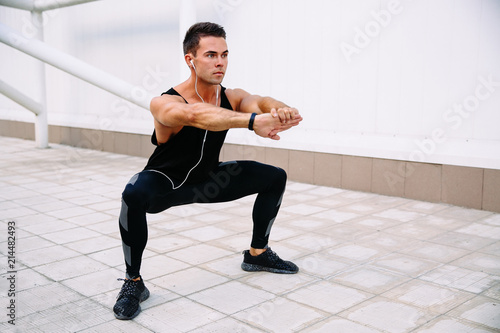 Attractive sportive man doing squats, outdoors