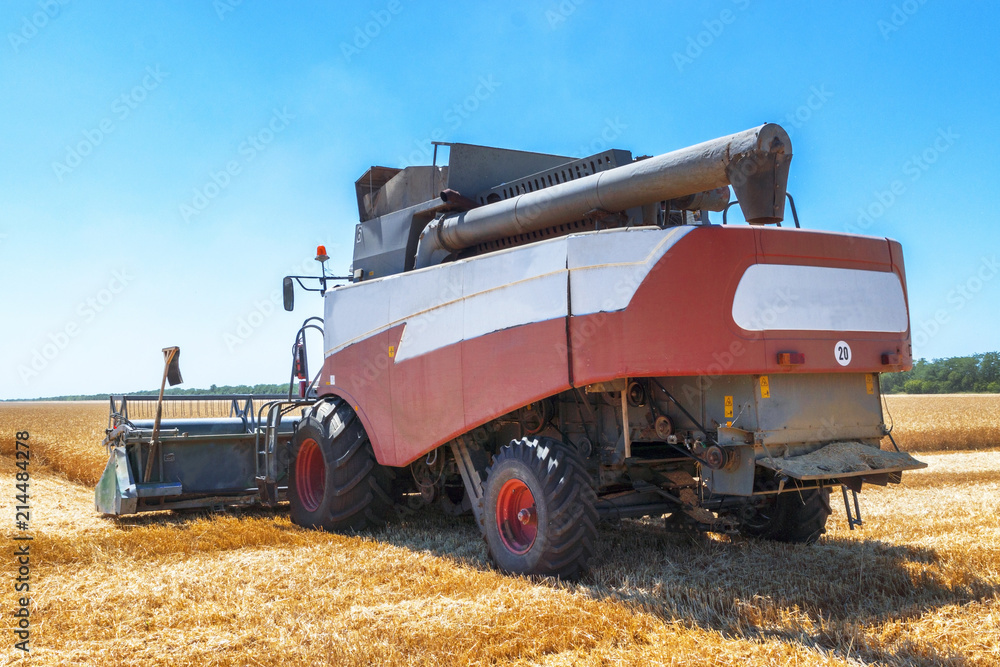 Obraz premium Harvester machine to harvest wheat field working. Combine harvester agriculture machine harvesting golden ripe wheat field. Agriculture