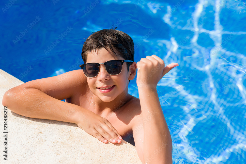Young child on holiday at the swimming pool by the beach pointing and showing with thumb up to the side with happy face smiling