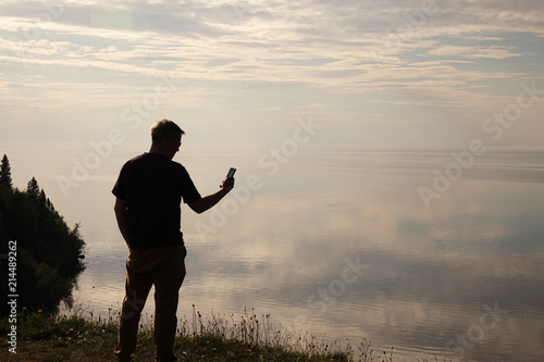 A man standing on top of a hill and looking at his mobile phone in his hands.Silhouette of the traveler.