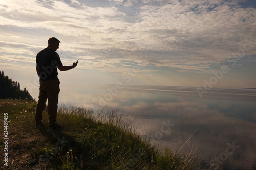 A man standing on top of a hill and looking at his mobile phone in his hands.Silhouette of the traveler.