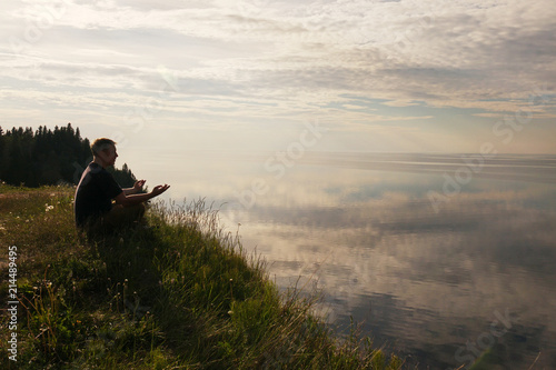 Man sitting in a Lotus position on top of a hill .