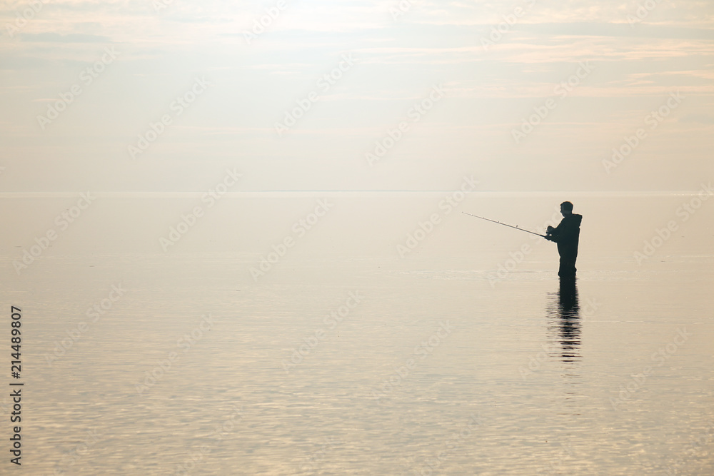 Silhouette of a fisherman at sunset. Fishing on the lake.