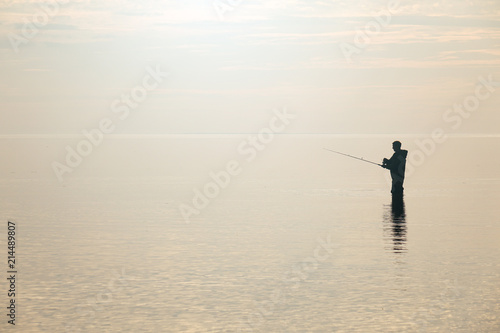 Silhouette of a fisherman at sunset. Fishing on the lake.