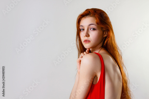 Young sexy slim woman in red swimsuit posing in studio. Full length fashion portrait of beautiful girl with long wavy red hair. Swimwear or bikini mode. Copy space, gray background