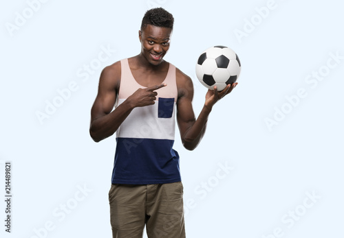 Young african american man holding soccer football ball very happy pointing with hand and finger