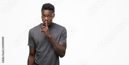 Young african american man wearing grey t-shirt asking to be quiet with finger on lips. Silence and secret concept. photo