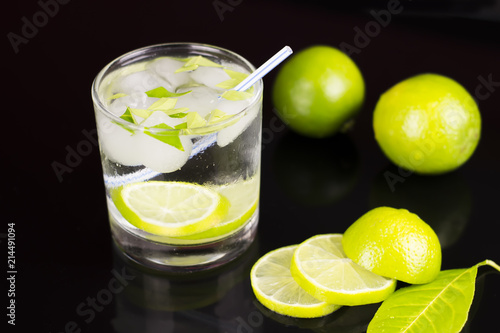 Alcohol drink (Gin Tonic cocktail) with lime and ice on black background with reflections