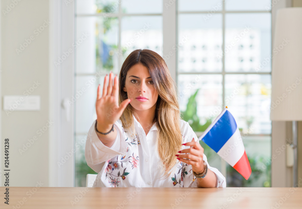 Young woman at home holding flag of France with open hand doing stop sign with serious and confident expression, defense gesture