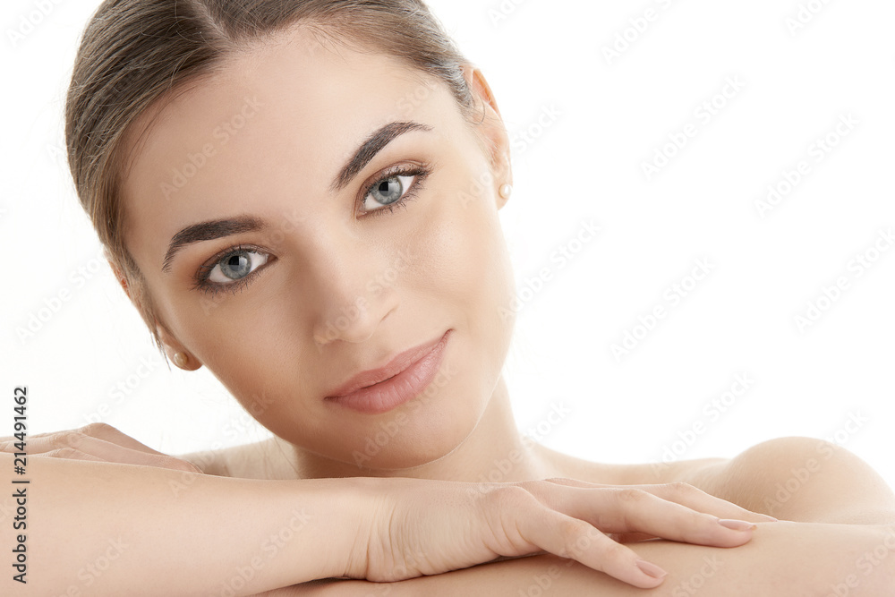 Portrait of a beautiful young woman with naked shoulders smiling while posing at isolated light blue background. Face beauty skin care. Natural make up Portrait of a beautiful young woman with naked shoulders smiling while posing at isolated light blue background. Face beauty skin care. Natural make up