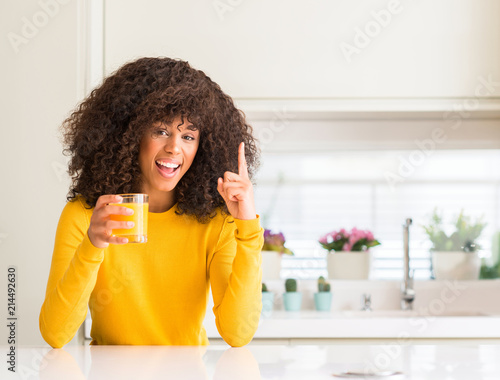 African american woman drinking orange juice in a glass surprised with an idea or question pointing finger with happy face  number one