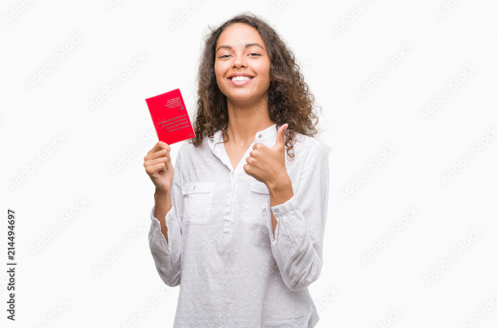 Young hispanic woman holding passport of Switzerland happy with big smile doing ok sign, thumb up with fingers, excellent sign Young hispanic woman holding passport of Switzerland happy with big smile doing ok sign, thumb up with fingers, excellent sign