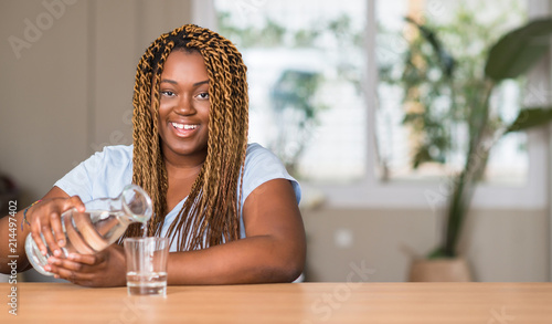 African american woman drinking water with a happy face standing and smiling with a confident smile showing teeth