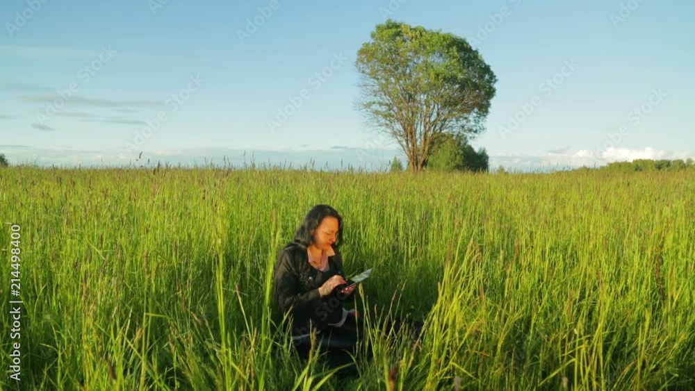Young woman working on a tablet in the park, she sits on a green grass overall plan Young woman working on a tablet in the park, she sits on a green grass overall plan