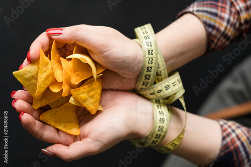 diet eating vs fast food. woman hands tied with measure tape. forbidden chips snack. healthy lifestyle choices