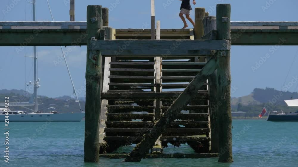 Legs of boy running through top and seagull flies past old wooden steps from wharf down to water at Russell in Bay Of Islands. Legs of boy running through top and seagull flies past old wooden steps from wharf down to water at Russell in Bay Of Islands.