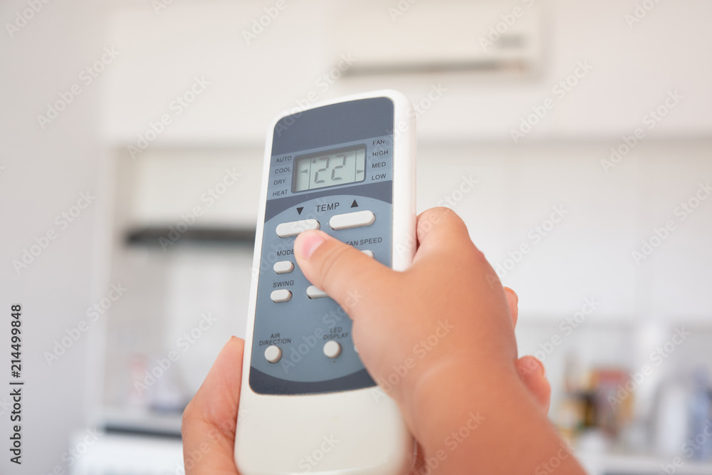children's hand turns on the air conditioner using the remote control.