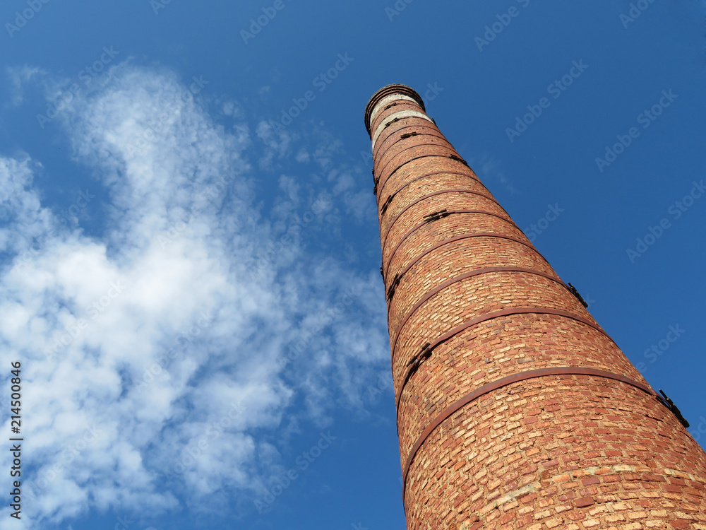 Red brick pipe on the background of the blue sky with white clouds, bottom view. Concept of environmentally friendly production