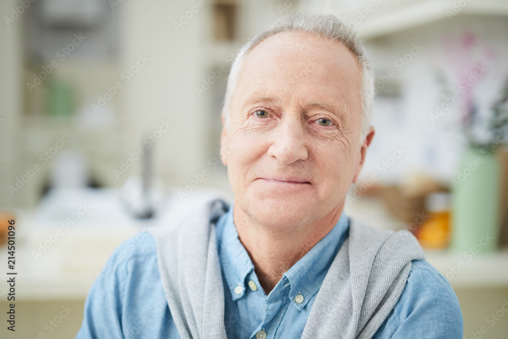 Mature grey-haired man in denim shirt looking at you while sitting in the kitchen - obrazy, fototapety, plakaty 