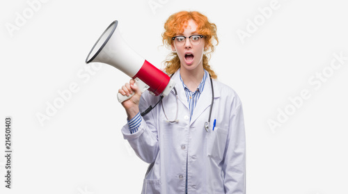 Young redhead doctor woman holding megaphone scared in shock with a surprise face, afraid and excited with fear expression