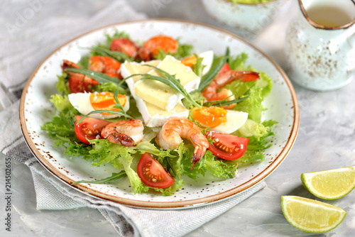 Healthy lettuce salad with arugula, large shrimps, cherry tomatoes, boiled egg, brie cheese and grated parmesan cheese.