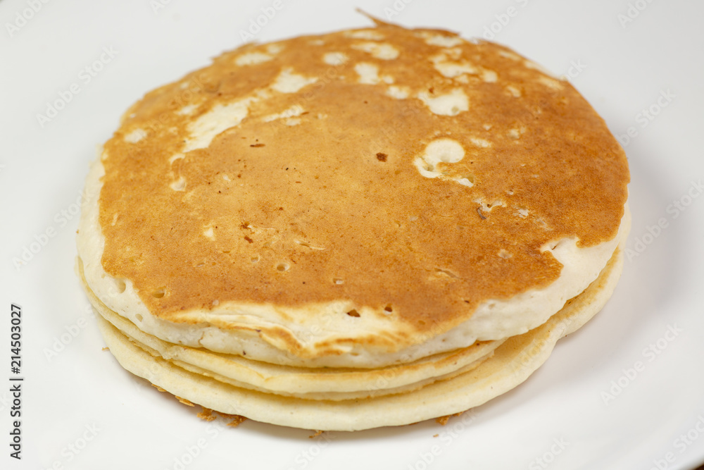 A stack of golden pancakes on a white plate sitting on a kitchen table waiting to be eaten