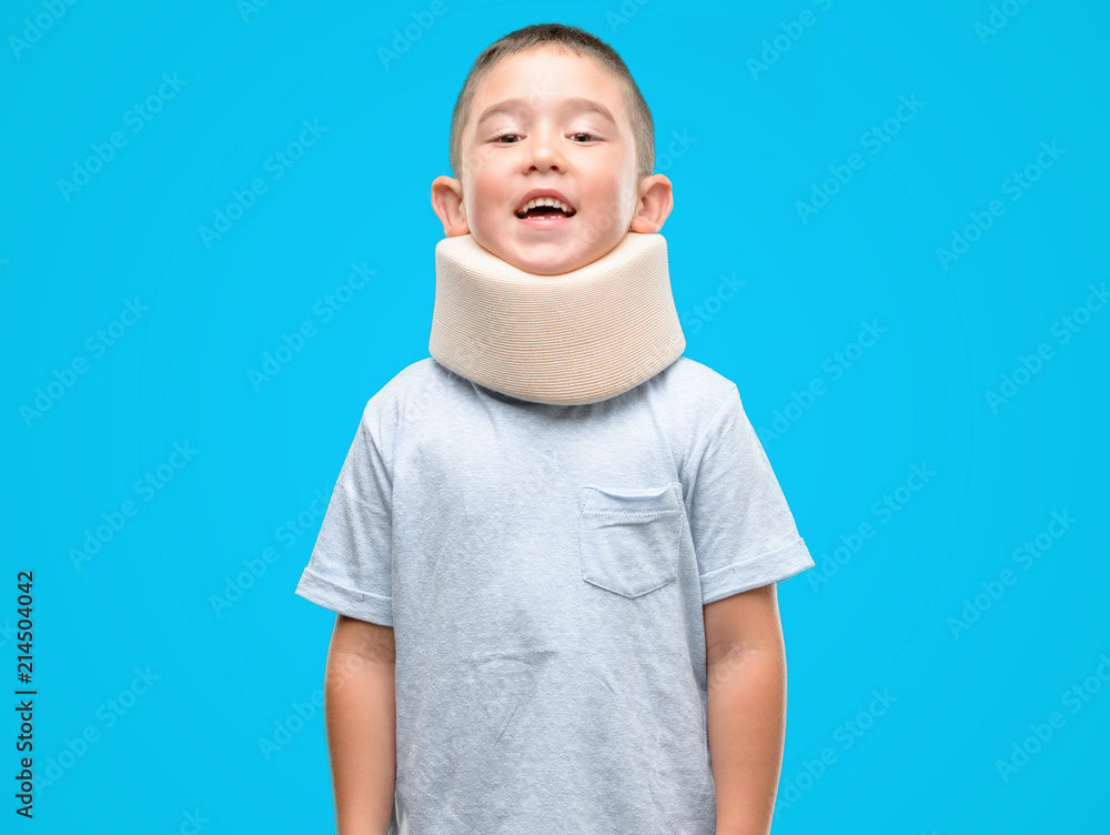 Dark haired little child injured wearing neck collar with a happy face standing and smiling with a confident smile showing teeth