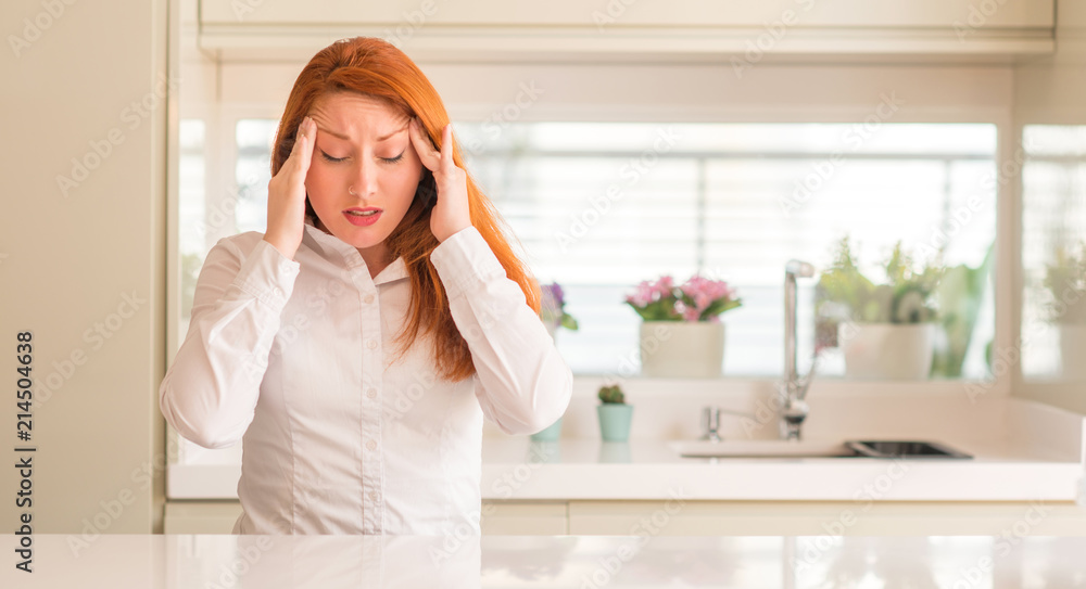 Redhead woman at kitchen with hand on head for pain in head because stress. Suffering migraine. Redhead woman at kitchen with hand on head for pain in head because stress. Suffering migraine.