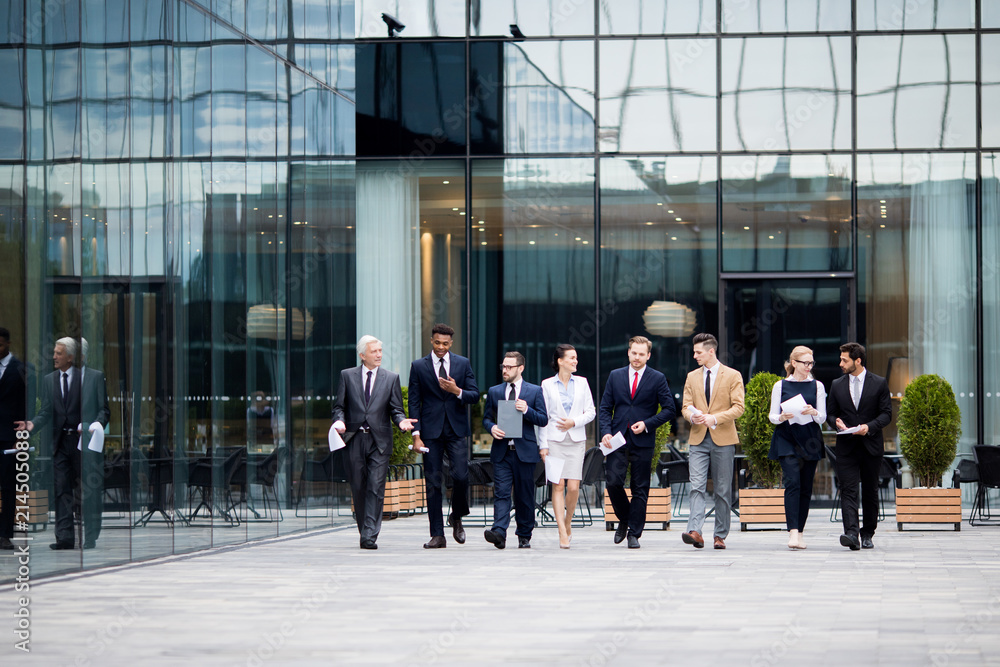 Obraz premium Large group of business people walking along modern business center and talking in urban environment