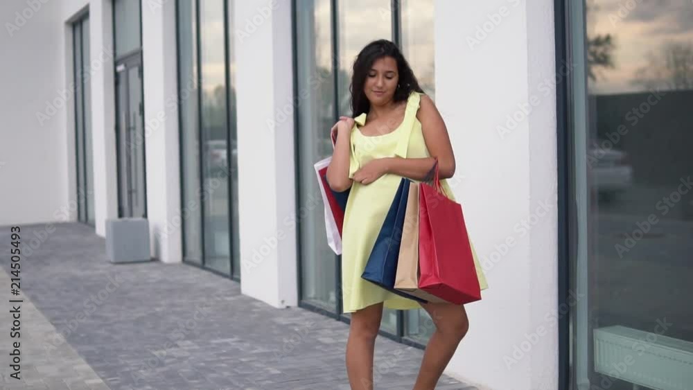 Beautiful girl model in a long dress after shopping with colored bags in hands having a good mood. slow motion. Beautiful girl model in a long dress after shopping with colored bags in hands having a good mood. slow motion.