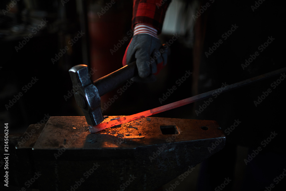 Gloved hand of blacksmith with hammer during work with hot red iron workpiece Gloved hand of blacksmith with hammer during work with hot red iron workpiece
