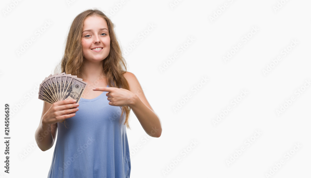 Young blonde woman holding dollars very happy pointing with hand and finger Young blonde woman holding dollars very happy pointing with hand and finger
