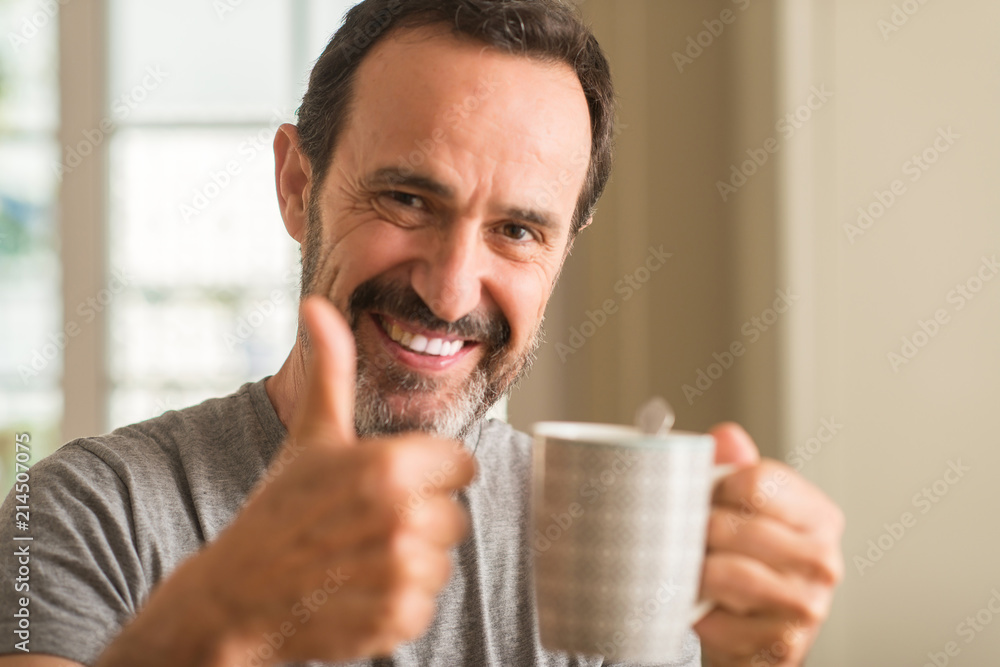 Middle age man drinking coffee in a cup happy with big smile doing ok sign, thumb up with fingers, excellent sign Middle age man drinking coffee in a cup happy with big smile doing ok sign, thumb up with fingers, excellent sign