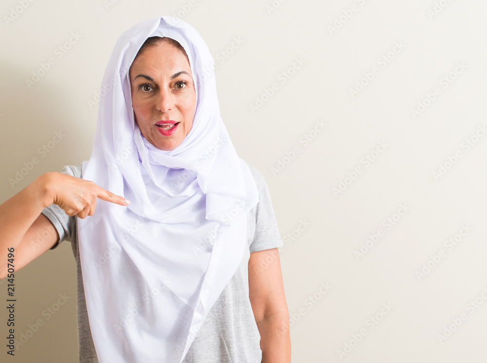 Middle age arabian woman wearing white hijab with surprise face pointing finger to himself Middle age arabian woman wearing white hijab with surprise face pointing finger to himself