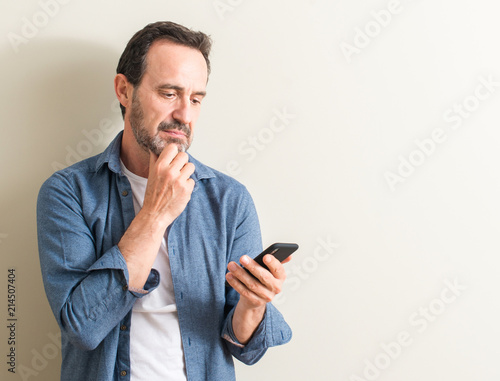 Fototapeta Senior man using smartphone serious face thinking about question, very confused idea