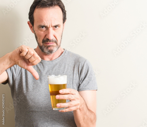 Senior man drinking beer with angry face, negative sign showing dislike with thumbs down, rejection concept