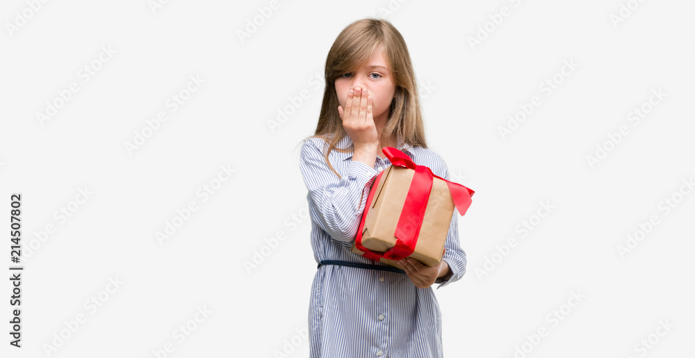 Young blonde toddler holding a present cover mouth with hand shocked with shame for mistake, expression of fear, scared in silence, secret concept Young blonde toddler holding a present cover mouth with hand shocked with shame for mistake, expression of fear, scared in silence, secret concept