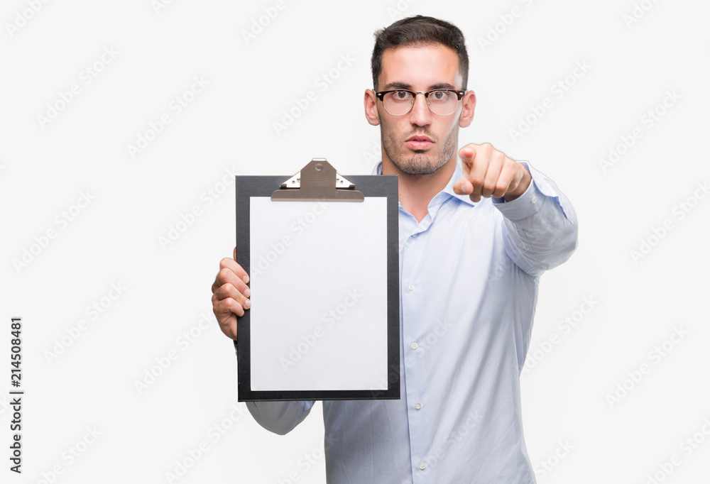 Handsome young business man showing a clipboard pointing with finger to the camera and to you, hand sign, positive and confident gesture from the front Handsome young business man showing a clipboard pointing with finger to the camera and to you, hand sign, positive and confident gesture from the front