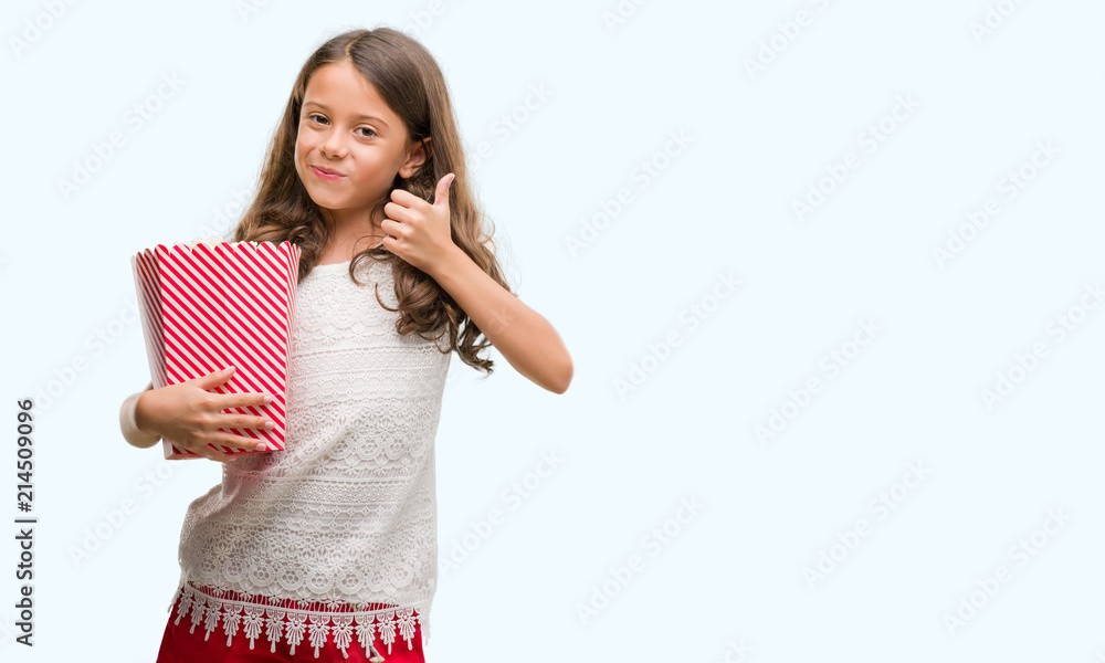 Brunette hispanic girl eating popcorn happy with big smile doing ok sign, thumb up with fingers, excellent sign