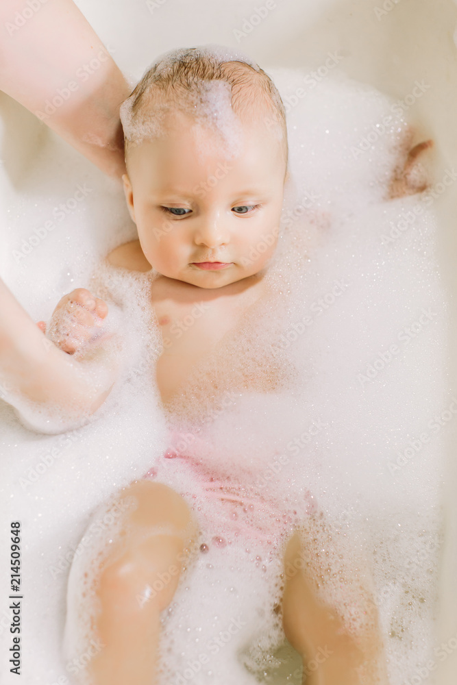 Happy laughing baby taking a bath playing with foam bubbles. Little child in a bathtub. Infant washing and bathing. Hygiene and care for young children. Adorable bath baby with soap suds on hair Happy laughing baby taking a bath playing with foam bubbles. Little child in a bathtub. Infant washing and bathing. Hygiene and care for young children. Adorable bath baby with soap suds on hair