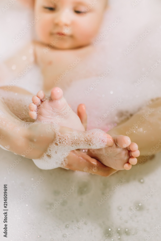 Fototapeta premium Happy laughing baby taking a bath playing with foam bubbles. Little child in a bathtub. Infant washing and bathing. Hygiene and care for young children. Adorable bath baby with soap suds on hair