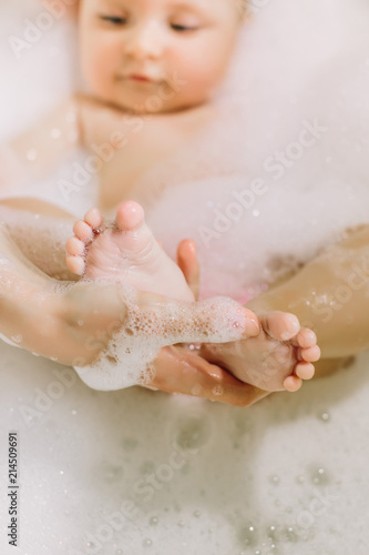 Happy laughing baby taking a bath playing with foam bubbles. Little child in a bathtub. Infant washing and bathing. Hygiene and care for young children. Adorable bath baby with soap suds on hair