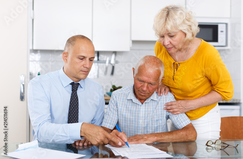 Elderly husband and wife signing agreement papers with bank worker