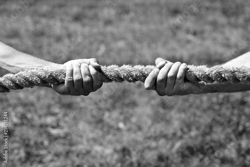 Two men's hands pull the rope each in his own direction. The concept of dispute, conflict and force. Black and white